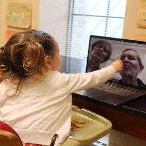 A young child points at a screen during a video chat.